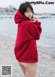 A woman in a red hoodie standing on a beach.