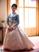 A woman in a blue and pink hanbok poses for a picture.