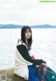 A woman sitting on a rock by the water.