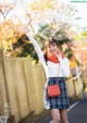 A woman in a white sweater and plaid skirt waving her hand.