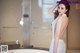 A woman in a white dress standing in front of a bathtub.