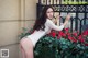 A woman in a white dress leaning against a fence with red roses.