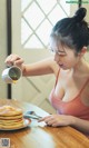 A woman pouring syrup on a stack of pancakes.