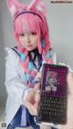 A girl with pink hair holding up a cell phone.