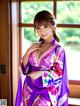 A woman in a purple kimono posing by a window.